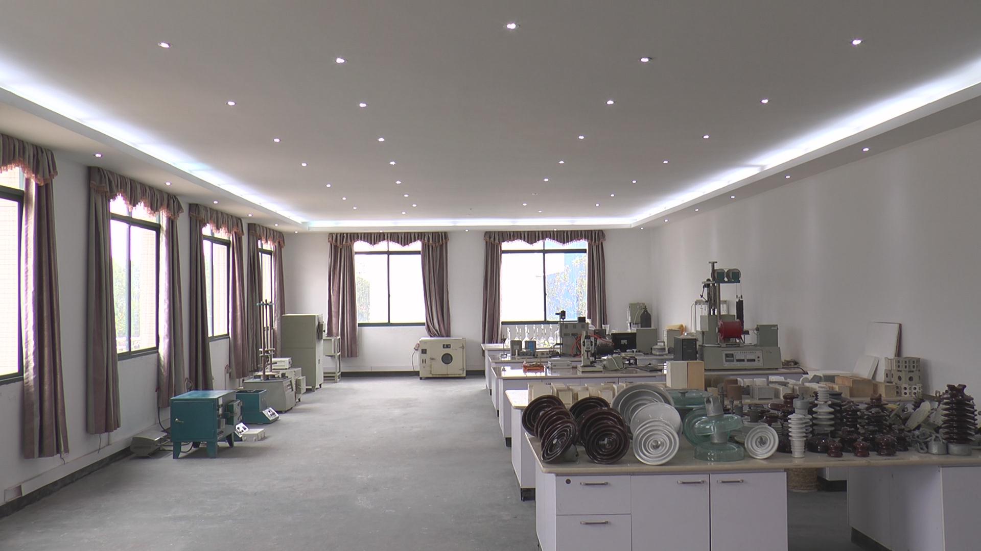 A bright empty showroom with curtained windows, recessed lights, and tables displaying items, in soft white and warm neutral tones.